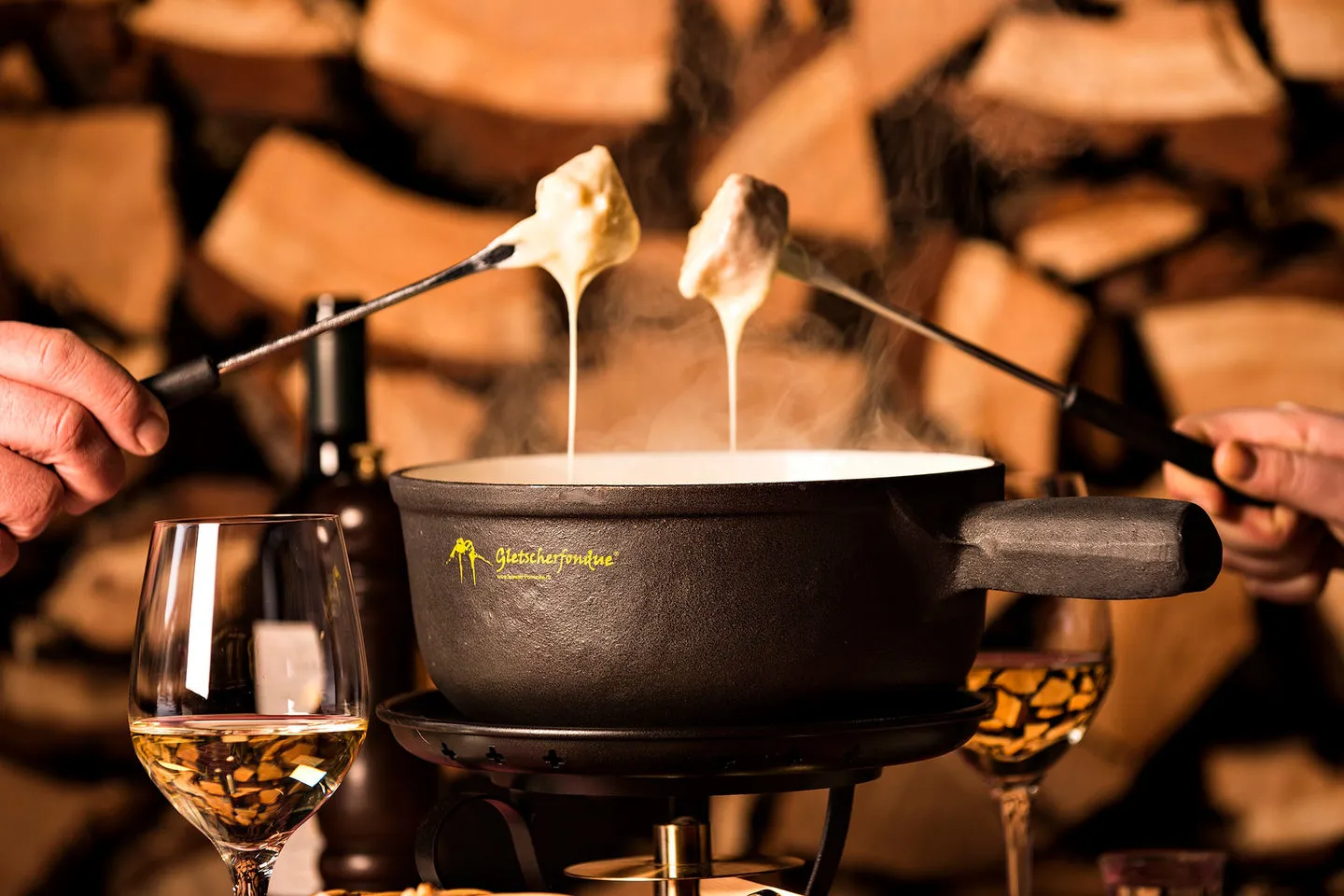 Käsefondue in Basel: Caquelon mit Gletscherfondue, zwei Gabeln mit Brot, Weissweingläser